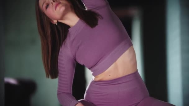 紫のスポーツスーツの若い女性がフィットネスをやって-フィットネスボールに座って横に傾いて — ストック動画