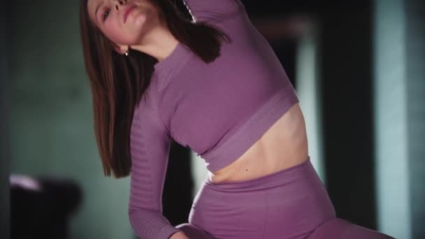 Giovane donna in tuta sportiva viola che fa fitness - seduta sulla palla fitness e appoggiata ai lati — Video Stock