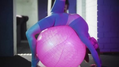 Mor spor takım elbiseli genç bir kadın spor yapıyor. Neon ışıklı spor topu ile egzersiz yapıyor.