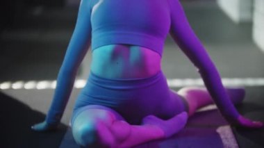 Spor takım elbiseli genç güzel bir kadın spor yapıyor. Neon mavi ışıklı yoga minderi üzerinde egzersiz yapıyor.