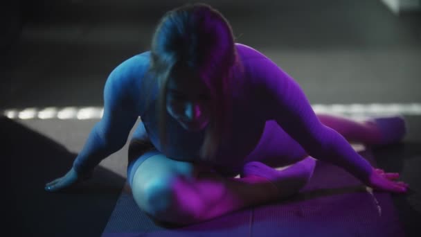 Mujer joven en traje deportivo púrpura haciendo fitness - haciendo ejercicios en esterilla de yoga con iluminación azul neón — Vídeos de Stock