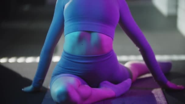 スポーツスーツの若いかなり女性がフィットネスを行う-ネオンブルーの照明でヨガマットで演習を行う — ストック動画