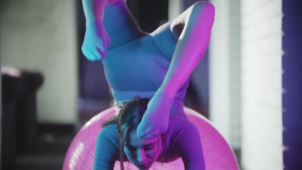 Mujer joven en traje deportivo púrpura haciendo fitness - haciendo ejercicios con pelota de fitness en luz azul neón — Vídeos de Stock