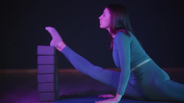 Junge Frau streckt ihr Bein mit der Ferse auf den Ständer - Neonbeleuchtung - blickt in die Kamera — Stockvideo