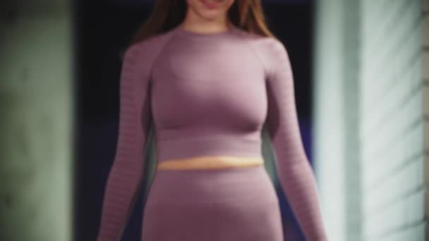 Jeune jolie femme en costume de sport violet marche vers l'avant à la caméra dans la salle de gym s'assoit sur le yoga et met ses cheveux en queue de cheval — Video