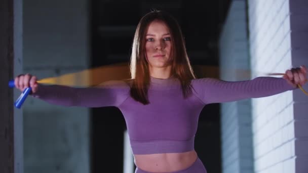 Молодая красивая женщина в фиолетовом спортивном костюме играет со скакалкой в руках и смотрит в камеру — стоковое видео