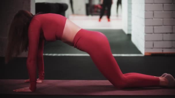 Mujer joven en traje deportivo rojo haciendo ejercicio en el gimnasio se pone de rodillas y dobla la espalda — Vídeos de Stock