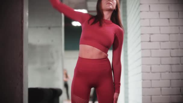Jonge vrouw in rood sportpak doet fitness oefeningen in de sportschool - opwarmen van haar lichaam — Stockvideo