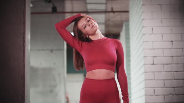 Kırmızı spor takım elbiseli genç bir kadın spor salonunda spor yapıyor. Boynunu ısıtıyor. — Stok video