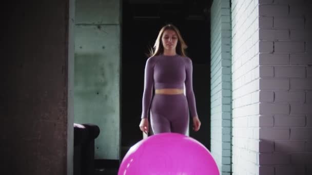 Mulher nova em terno de esportes roxo que faz a aptidão - senta-se na bola de fitness — Vídeo de Stock