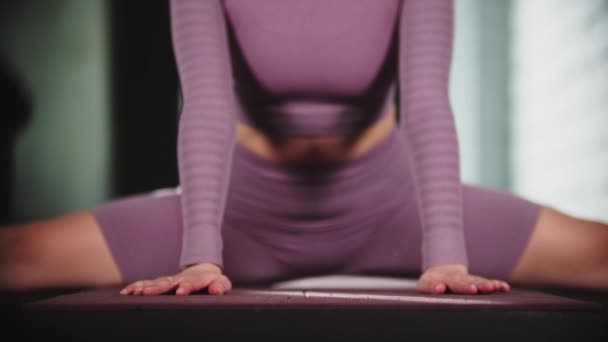 Spor salonunda jimnastik yapan genç bir kadın - bölmelere oturur ve öne doğru eğilir - kameraya bakar — Stok video