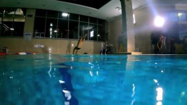 Genç adam arkadan suya atlıyor ve ileri doğru gülümsüyor.