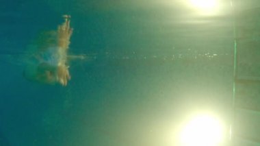 Su geçirmez bardaklı genç adam su altında yüzüyor - hızla ayaklarını yana doğru itiyor ve geri dönüyor.