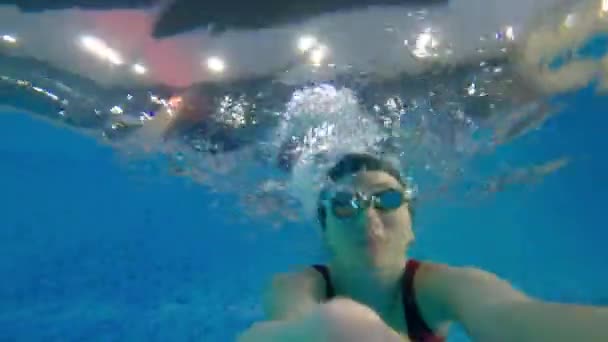 Mujer joven sumergirse en el agua sosteniendo una cámara y agitando su mano bajo el agua — Vídeos de Stock