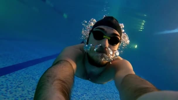 Young man in waterproof glasses swimming underwater holding a camera — Stockvideo