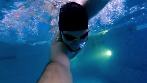 Junger Mann mit wasserdichter Brille schwimmt unter Wasser und hält eine Kamera in der Hand — Stockvideo