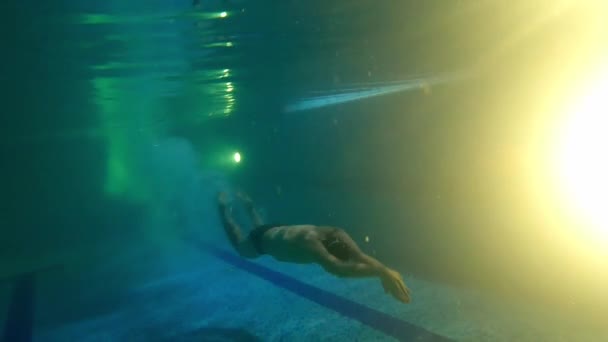 Młody człowiek pływający pod wodą blisko dna basenu — Wideo stockowe