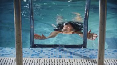 Yüzme sporları. Genç bir yüzücü merdivenin üstündeki havuzda sudan çıkar.