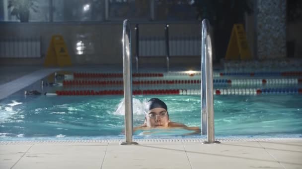 Deportes de natación - nadador joven sale de la piscina con la escalera y mira a la cámara — Vídeo de stock