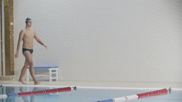 Swimming sports - young man swimmer puts on the glasses and dives in the pool — 图库视频影像