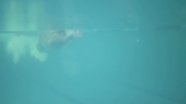 Genç adam ayaklarını yana doğru itiyor ve suyun altında geri dönüyor.