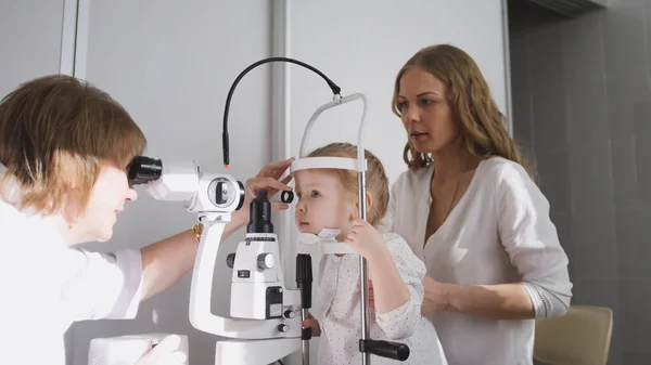 Kleines Mädchen und ihre Mama in der Augenheilkunde - Augenoptiker überprüft das Sehvermögen kleiner Kinder — Stockfoto