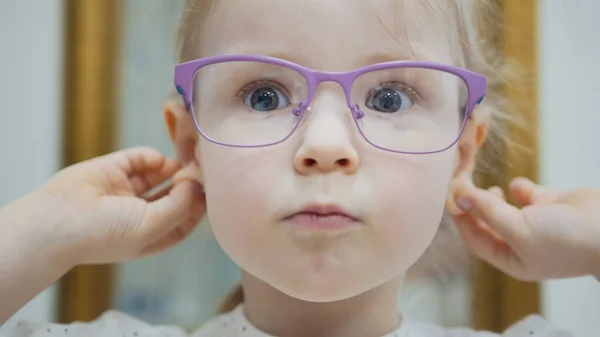 Kleines Mädchen probiert modische Brille in der Nähe des Spiegels - Einkaufen in Augenklinik — Stockfoto