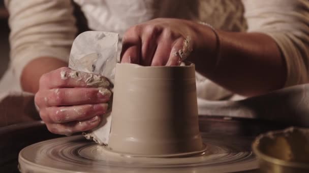 Çömlek atölyesi - genç kadın çömlekçinin tencerenin kenarlarını bir aletle düzleştiriyor — Stok video