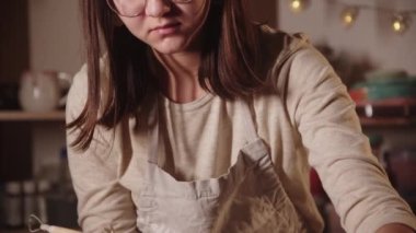 Genç bayan çömlekçi bir aletle ıslak tencerenin kenarlarını yapıyor.