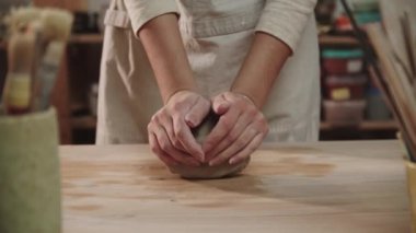 Kadın çömlekçi sanat stüdyosundaki masaya kil yoğuruyor.