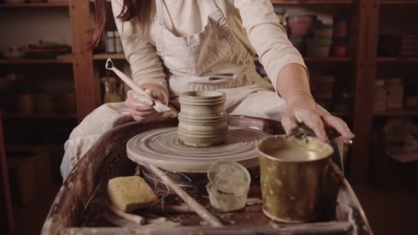 Young woman shaping a pot out of wet clay using an instrument — Vídeo de Stock