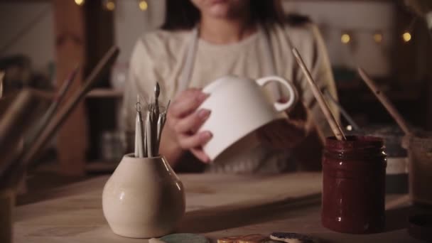 Genç bayan çömlekçi büyük beyaz seramik çay fincanını inceliyor. — Stok video