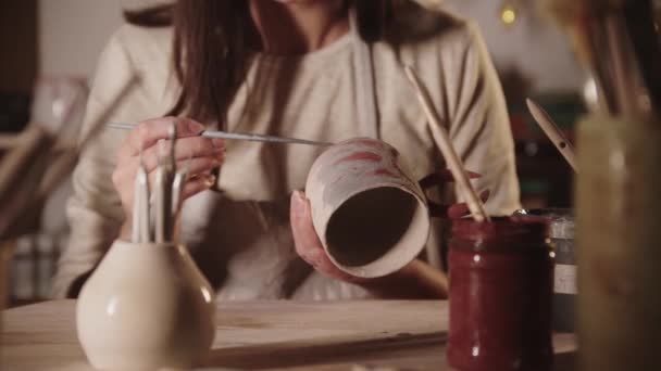 Jonge vrouw pottenbakker kleuren keramische product met een borstel kijkt dan in de camera — Stockvideo