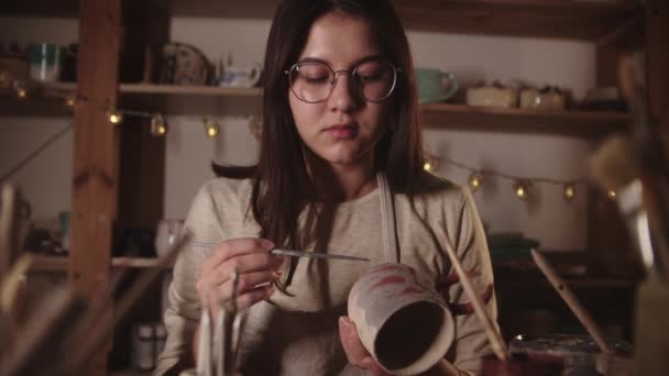 Young woman in art studio coloring ceramic product with a brush then looks in the camera — Vídeo de Stock