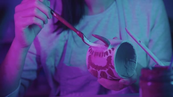 Seramik bardağa resim yapan genç bir kadın. Sanat stüdyosunda fırçayla. Neon ışıklı. — Stok video