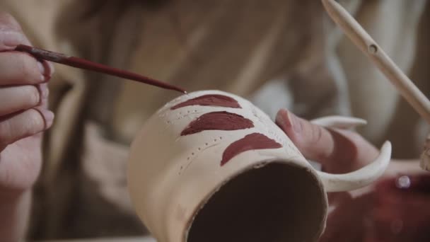 Young woman potter painting on the ceramic cup with a brush and red color — 图库视频影像
