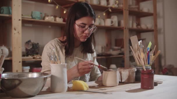 Sanat stüdyosunda çalışan genç bayan çömlekçi masanın yanındaki seramik ürünü bitiriyor. — Stok video