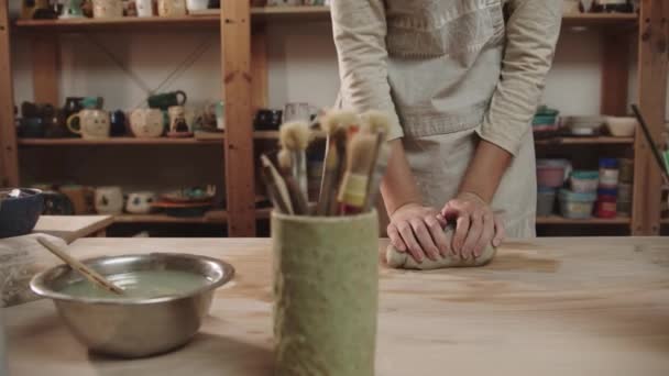Female potter kneads clay on the table in art studio - brushes and other tools standing on the foreground — Vídeo de Stock