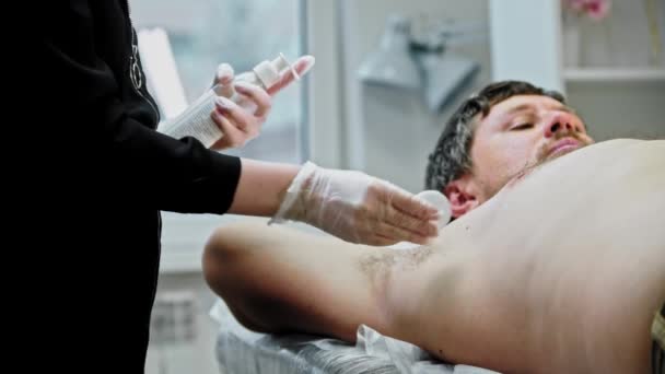 The epilation master disinfects the male armpit with a cream — Stock videók