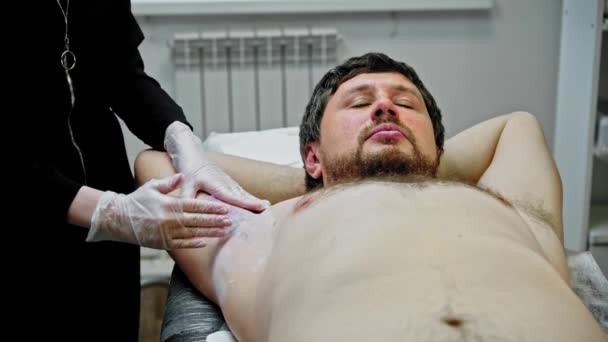 A man lying on a couch on waxing procedure — Stockvideo