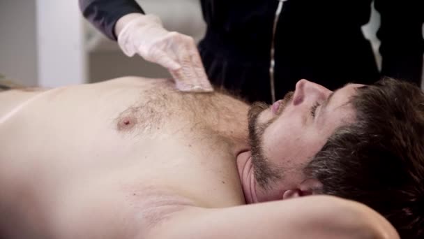 Waxing procedure - the master degreasing the chest of her male client — Stockvideo