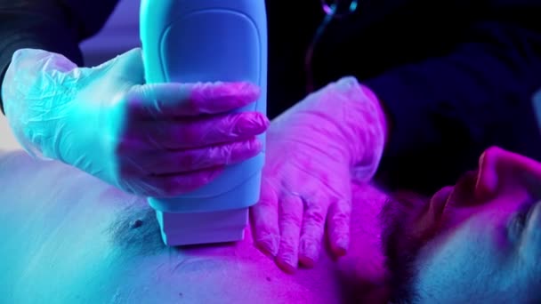 Procedura woskowania - mistrz nakładający gorący wosk na klatkę piersiową jej męskiego klienta - oświetlenie neonowe — Wideo stockowe