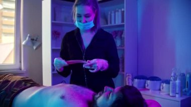 Ağda işlemi - usta neon ışıklı bir şerit kullanarak erkek müşterisinin göğsüne ağda yapıyor