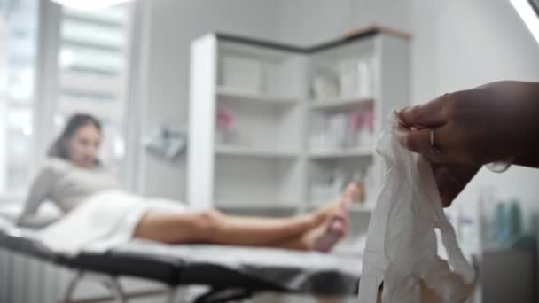 The epilation master puts on latex gloves before the procedure with a woman — Video Stock