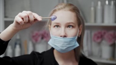 Sarışın tüy dökücü ustası spatuladaki sıcak mor balmumuna bakar.