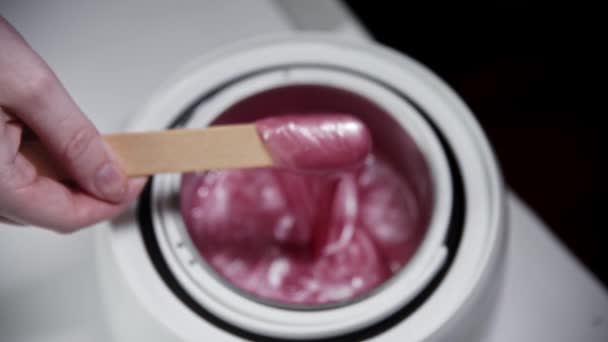Depilation master melts pink wax in the heater and mixing it using a spatula — Stock Video