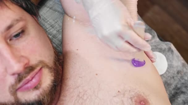 Wasprocedure - bebaarde man liggend op een bank en de meester die paarse was op zijn oksel aanbrengt — Stockvideo