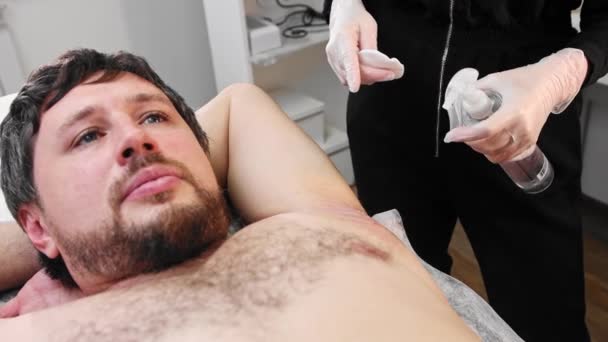 Waxing procedure - bearded man lying on a couch and the master cleanses the skin of wax residues — Video Stock