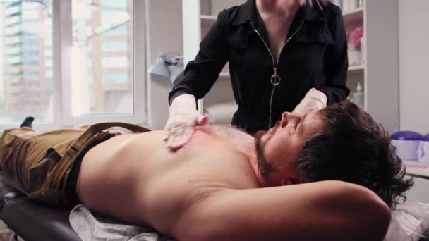 Waxing procedure - man lying on a couch and the master cleanses the skin on his chest of wax residues — Video Stock