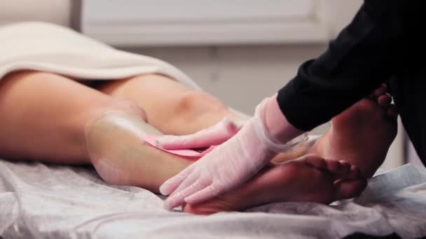 Waxprocedure - de meester onthaart vrouwenbenen met behulp van waxbanden — Stockvideo